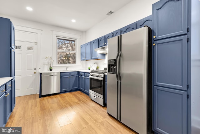 kitchen with blue cabinetry, light countertops, appliances with stainless steel finishes, light wood-style floors, and under cabinet range hood