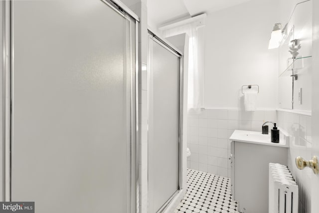 full bath with a stall shower, tile walls, vanity, and radiator heating unit