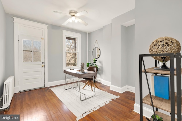 office space with radiator, a ceiling fan, baseboards, and dark wood-type flooring