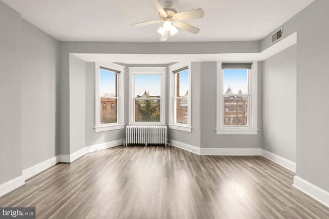 spare room with radiator heating unit, visible vents, baseboards, and wood finished floors