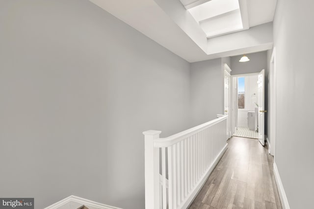 corridor featuring baseboards, wood finished floors, and an upstairs landing