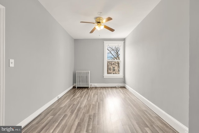 empty room with baseboards, light wood finished floors, a ceiling fan, and radiator