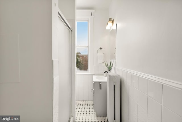 full bath with a shower with shower door, a wainscoted wall, tile walls, and vanity