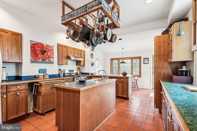 kitchen featuring stainless steel gas range oven, light tile patterned flooring, under cabinet range hood, a sink, and a center island with sink