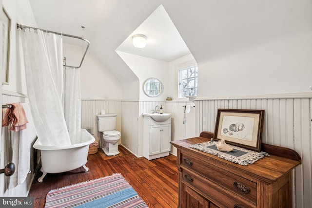 bathroom featuring lofted ceiling, toilet, wood finished floors, vanity, and wainscoting