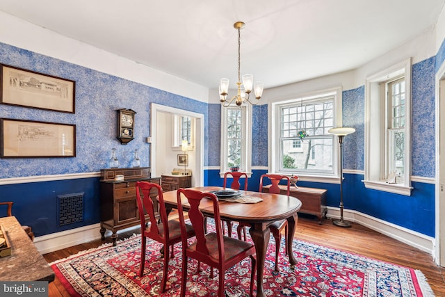 dining area featuring wallpapered walls, baseboards, visible vents, wood finished floors, and an inviting chandelier