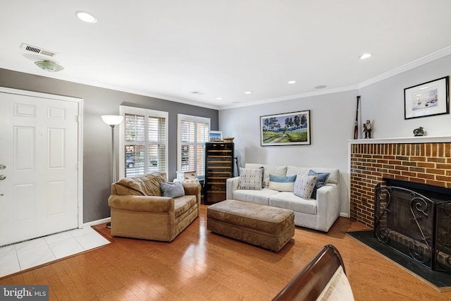 living room featuring crown molding, recessed lighting, visible vents, light wood-style flooring, and a brick fireplace