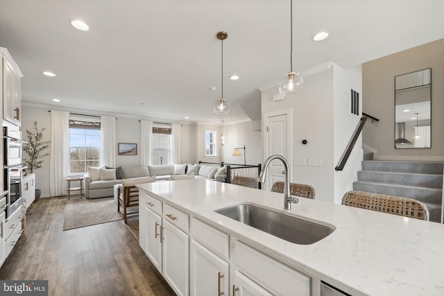 kitchen with a sink, white cabinets, open floor plan, light stone countertops, and pendant lighting