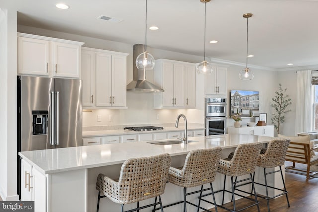 kitchen featuring stainless steel appliances, decorative light fixtures, a sink, and a center island with sink