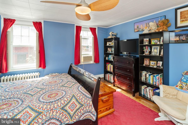 bedroom featuring hardwood / wood-style flooring, ornamental molding, radiator, and multiple windows