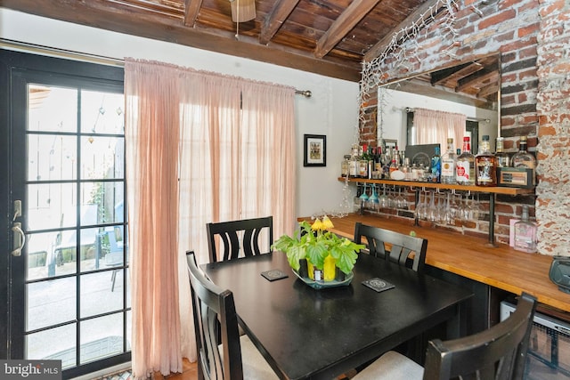 dining area featuring indoor bar, wood ceiling, beam ceiling, and brick wall