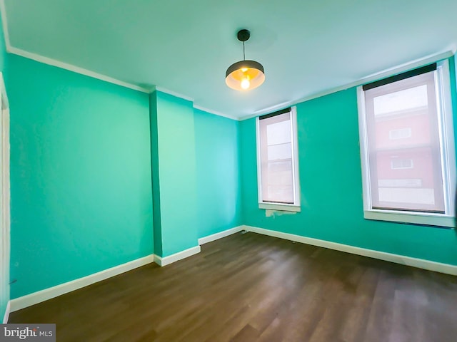 unfurnished room with crown molding, dark wood finished floors, and baseboards