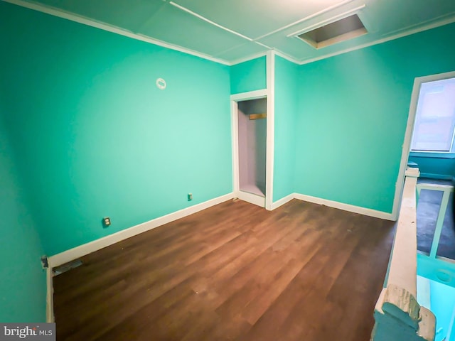 empty room with attic access, dark wood-style flooring, crown molding, and baseboards