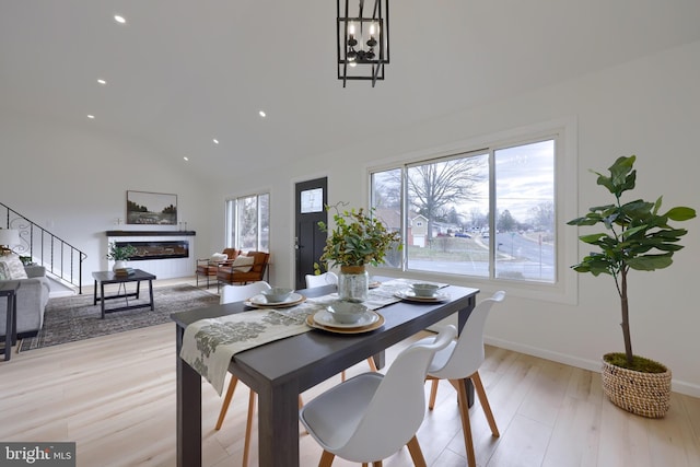 dining space with baseboards, a glass covered fireplace, lofted ceiling, stairs, and light wood-type flooring