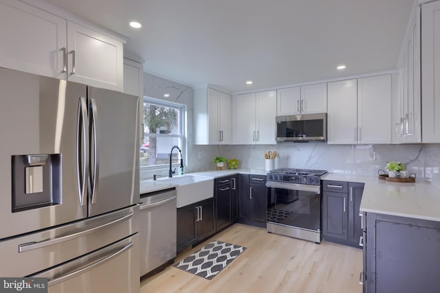 kitchen with white cabinets, appliances with stainless steel finishes, backsplash, light stone counters, and a sink