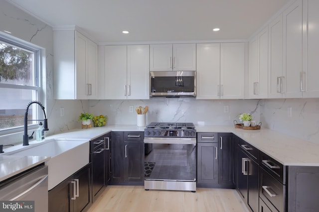 kitchen with light stone counters, appliances with stainless steel finishes, light wood-style floors, white cabinetry, and a sink