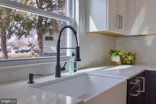 interior details with backsplash, light stone counters, white cabinets, and a sink