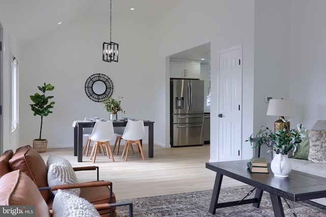 living room featuring baseboards, high vaulted ceiling, an inviting chandelier, and light wood-style floors