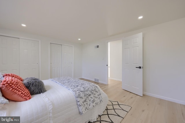 bedroom with light wood-type flooring, two closets, visible vents, and baseboards