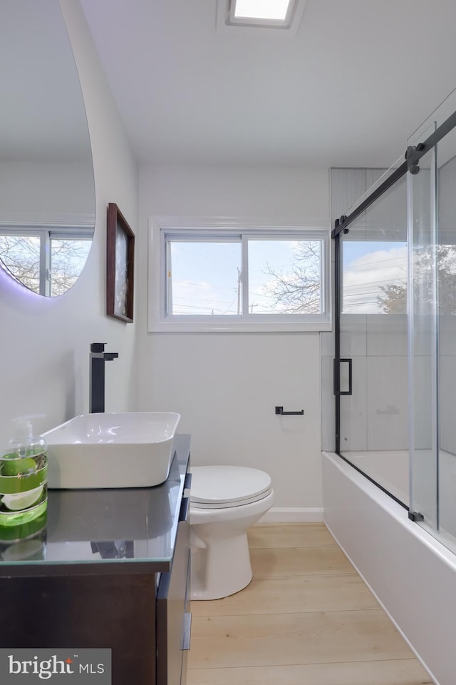 full bath featuring combined bath / shower with glass door, plenty of natural light, toilet, and wood finished floors