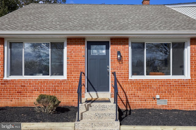 doorway to property featuring a shingled roof, crawl space, and brick siding