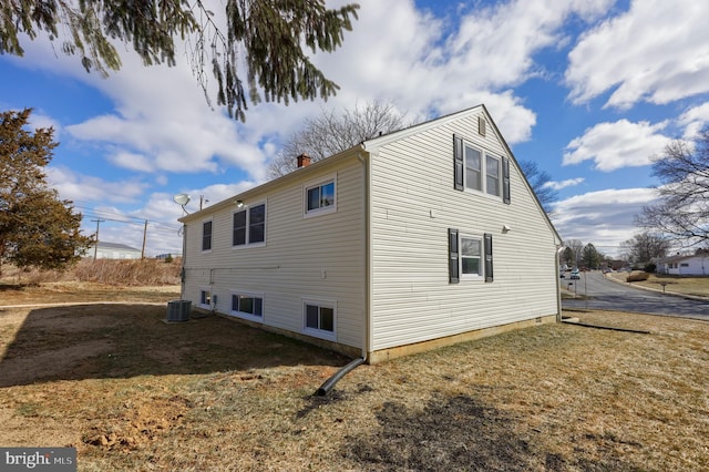 view of side of home featuring a yard, a chimney, and cooling unit