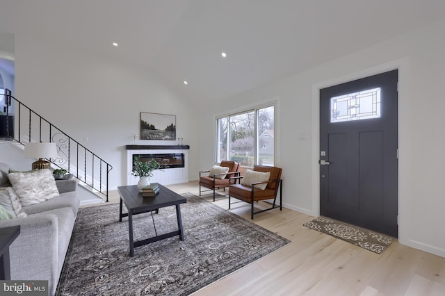 foyer entrance with light wood finished floors, baseboards, a glass covered fireplace, lofted ceiling, and stairs