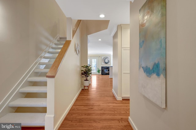 corridor with light wood-type flooring, stairway, baseboards, and recessed lighting