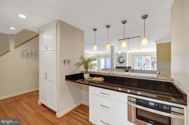 kitchen with pendant lighting, light wood-type flooring, white cabinets, and oven