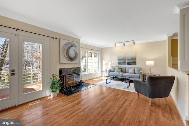 living area featuring rail lighting, visible vents, light wood-style flooring, a premium fireplace, and ornamental molding