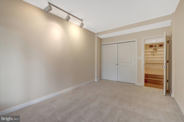 unfurnished bedroom featuring light carpet, track lighting, a closet, and baseboards