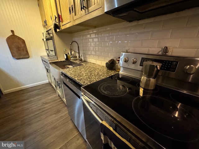 kitchen featuring appliances with stainless steel finishes, sink, backsplash, light stone countertops, and dark wood-type flooring