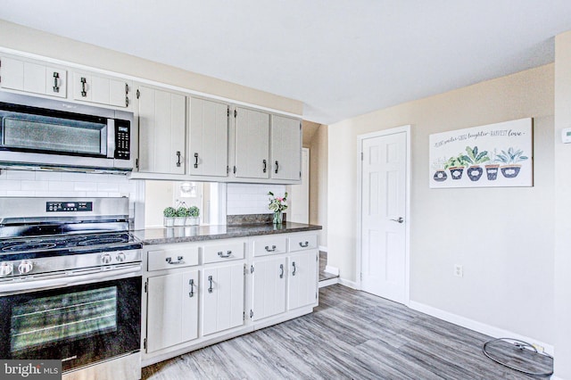 kitchen with light wood-type flooring, stainless steel appliances, white cabinetry, and backsplash