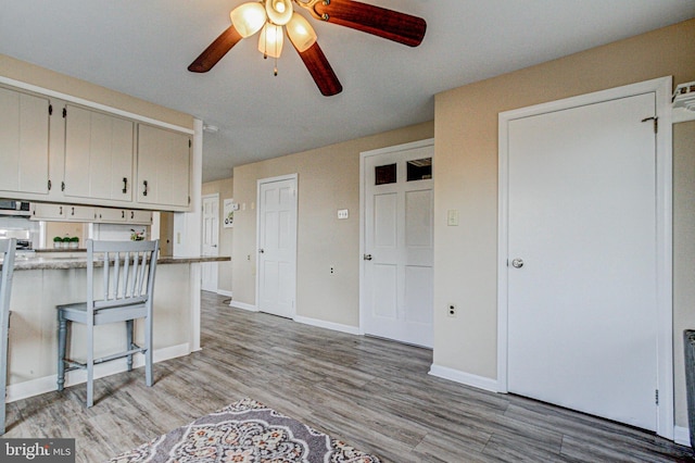 kitchen featuring ceiling fan, light hardwood / wood-style flooring, a kitchen breakfast bar, and white cabinets