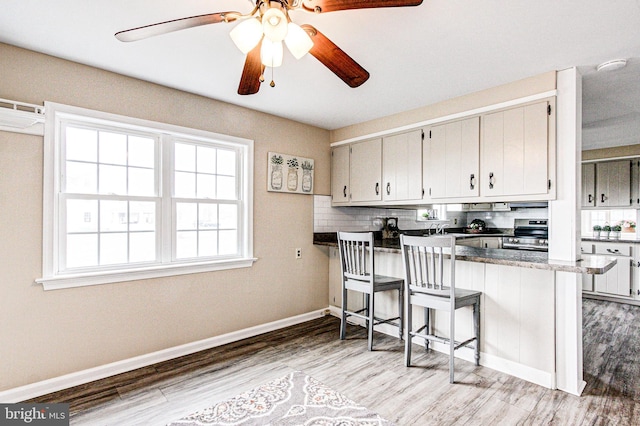 kitchen featuring stainless steel range with electric cooktop, kitchen peninsula, wood-type flooring, and a breakfast bar area