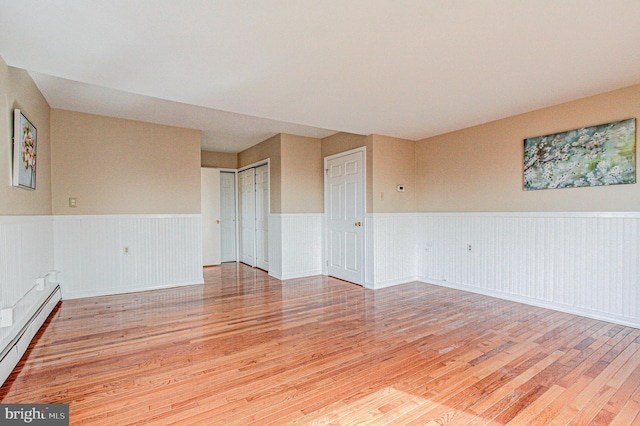 empty room with baseboard heating and light hardwood / wood-style flooring