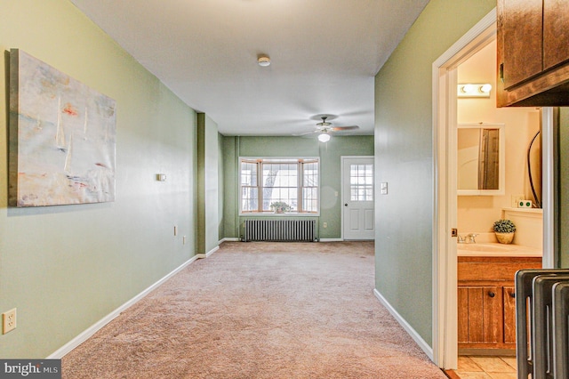 hallway featuring sink, light colored carpet, and radiator heating unit