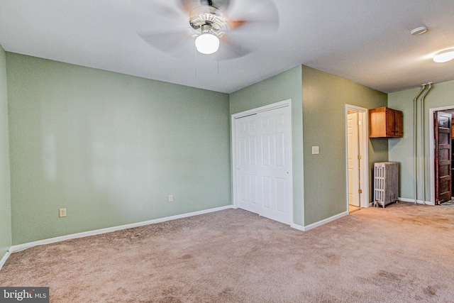 unfurnished bedroom with light carpet, radiator heating unit, ceiling fan, and a closet