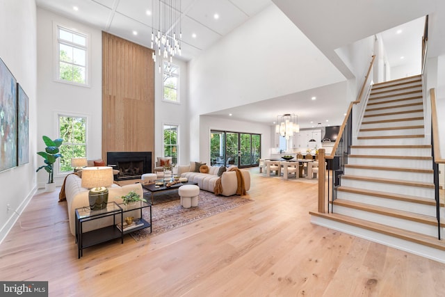 living room featuring an inviting chandelier, a large fireplace, light hardwood / wood-style floors, and a towering ceiling