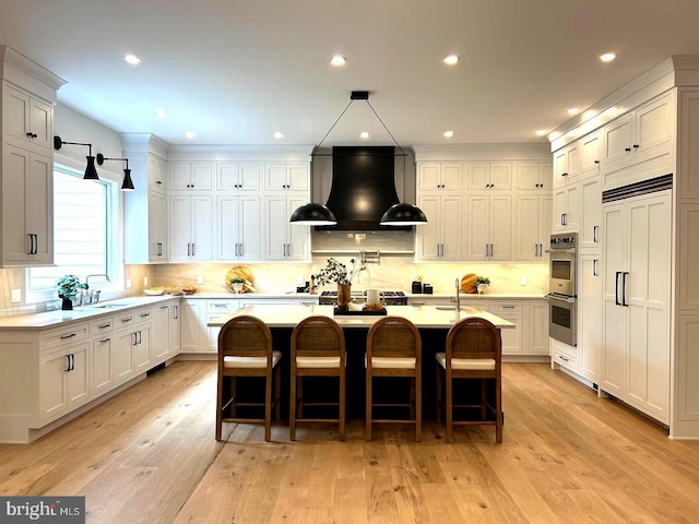 kitchen featuring wall chimney exhaust hood, a kitchen bar, light hardwood / wood-style flooring, a center island with sink, and white cabinets