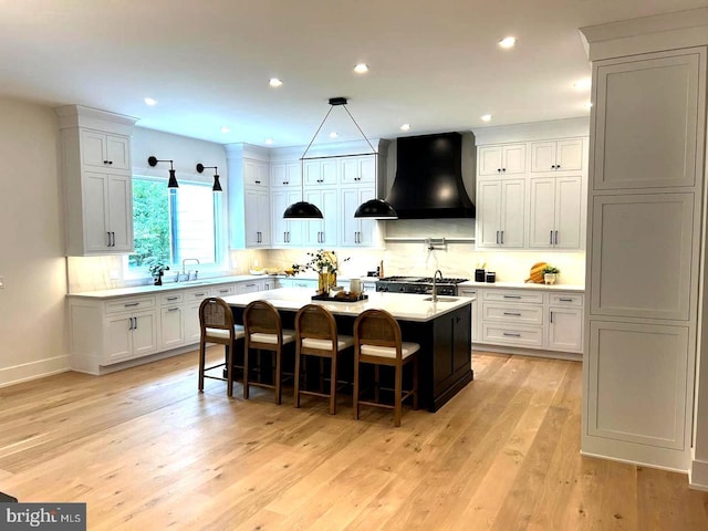 kitchen with white cabinetry, wall chimney exhaust hood, a breakfast bar, and a center island with sink