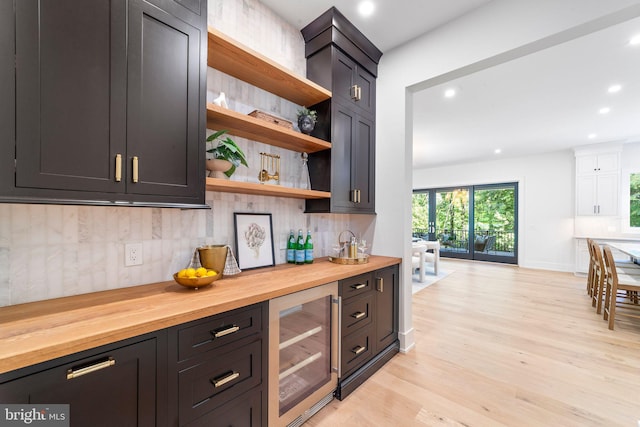 bar with backsplash, beverage cooler, butcher block countertops, and light hardwood / wood-style floors