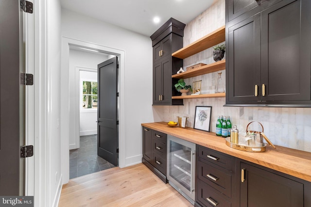 bar with wood counters, beverage cooler, light hardwood / wood-style flooring, and backsplash