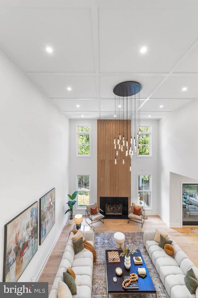 living room featuring coffered ceiling, hardwood / wood-style flooring, a fireplace, and a towering ceiling