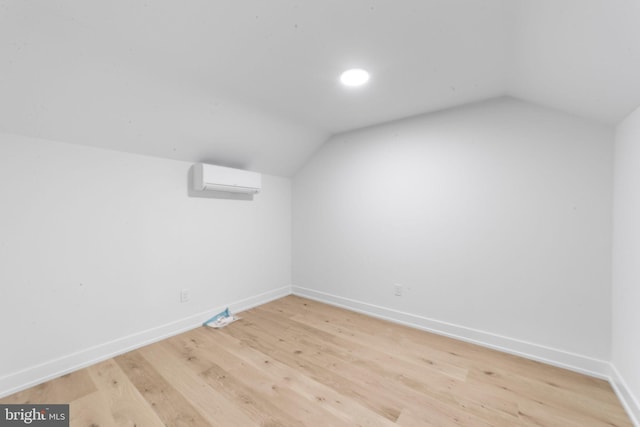 additional living space featuring lofted ceiling, hardwood / wood-style flooring, and an AC wall unit