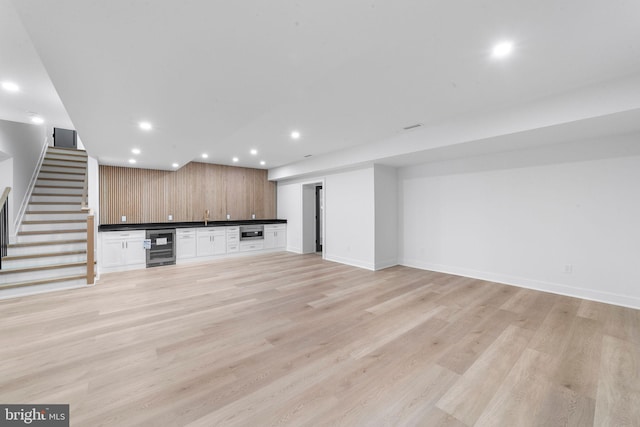 unfurnished living room with light hardwood / wood-style flooring, beverage cooler, and indoor bar