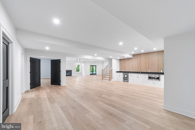 unfurnished living room featuring indoor bar, wine cooler, and light hardwood / wood-style flooring