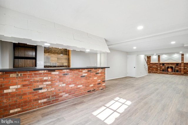 bar featuring brick wall, a brick fireplace, beamed ceiling, and light hardwood / wood-style floors