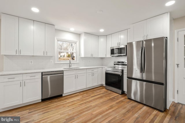 kitchen featuring light hardwood / wood-style flooring, tasteful backsplash, stainless steel appliances, white cabinets, and sink