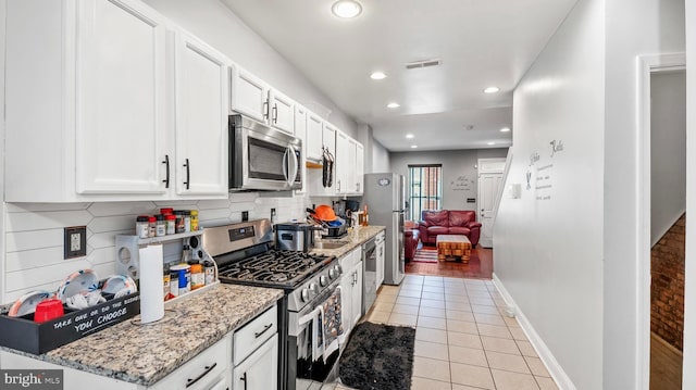 kitchen featuring light tile patterned flooring, stainless steel appliances, light stone countertops, and white cabinets